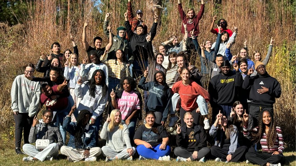 a large group of student outdoors raising up their hands